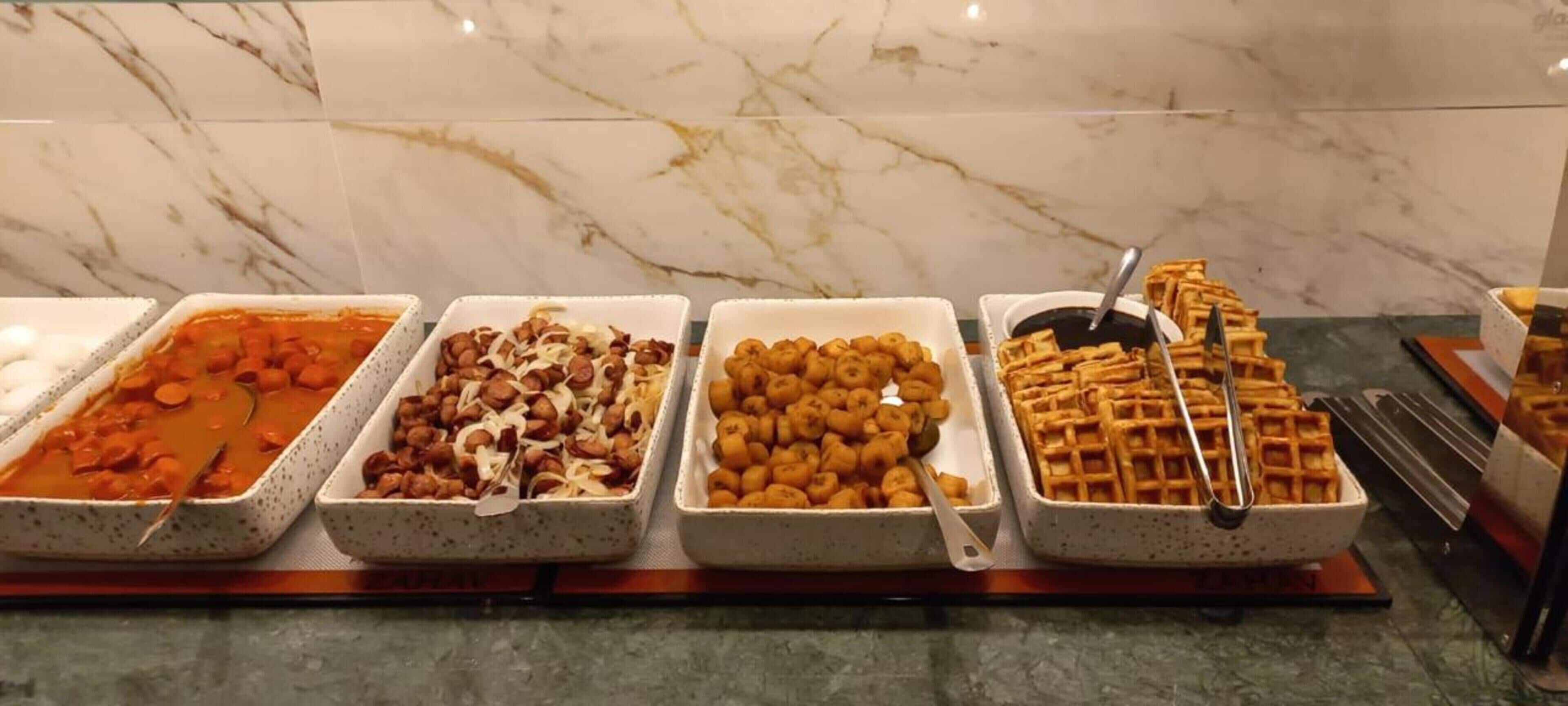 A buffet with various food items including a red sauce, nuts, fritters, and waffles.