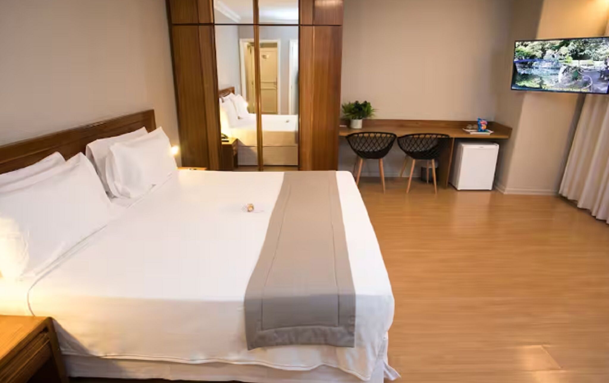 Habitación de hotel con cama, escritorio, dos sillas, refrigerador pequeño y televisor montado en la pared.