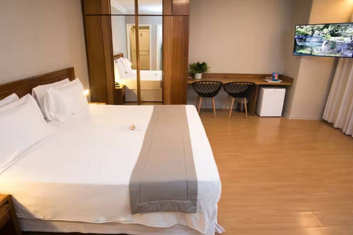 Habitación de hotel con cama, escritorio, dos sillas, refrigerador pequeño y televisor montado en la pared.