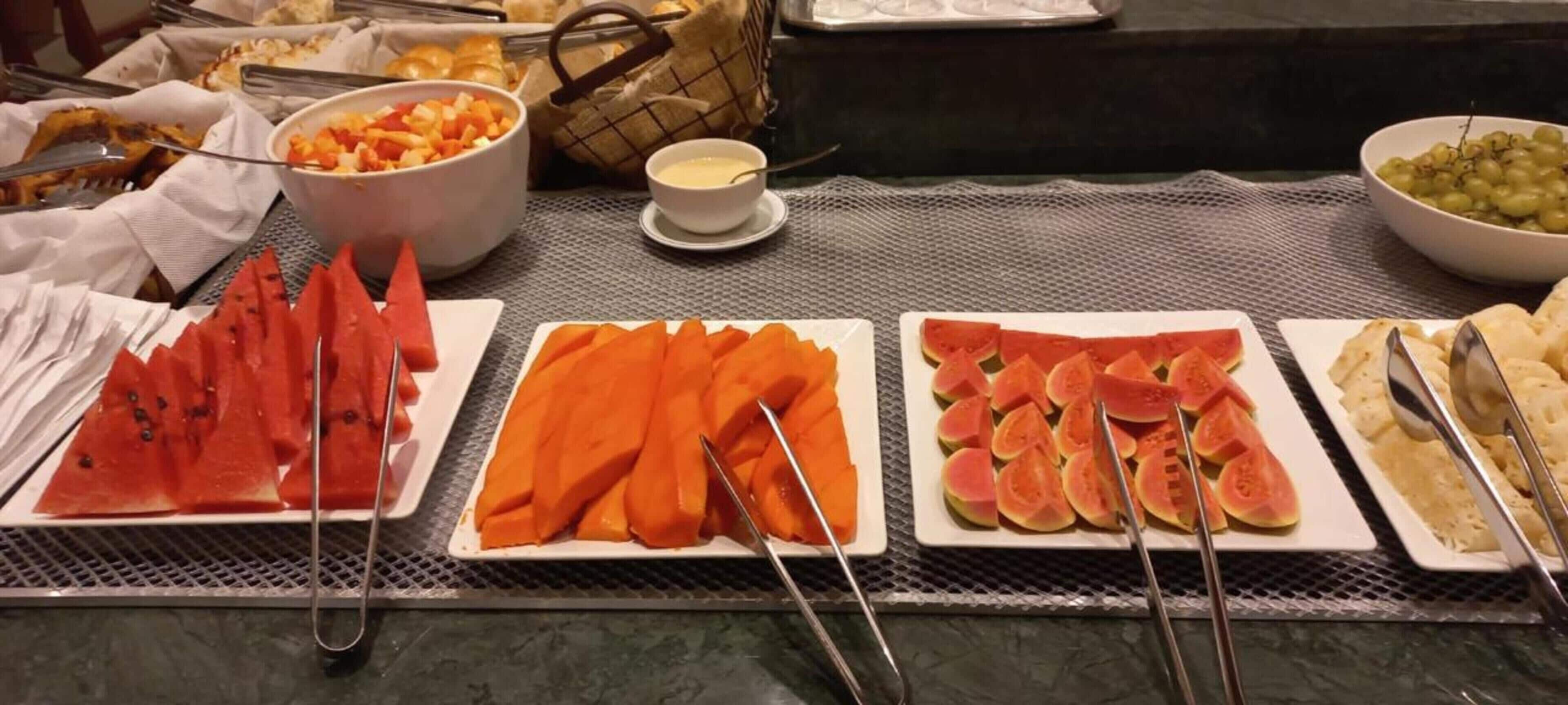 A buffet table with various fruits and vegetables, including watermelon, carrots, and figs, arranged on plates.