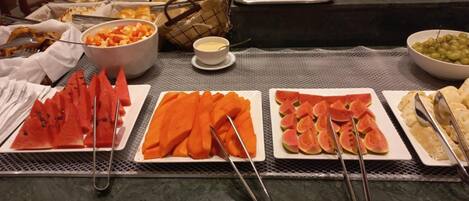 A buffet table with various fruits and vegetables, including watermelon, carrots, and figs, arranged on plates.