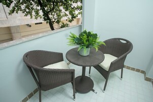 Ein Balkon mit zwei Korbstühlen, einem kleinen Tisch, einem Blumentopf und Blick auf ein Gebäude und einen Baum.