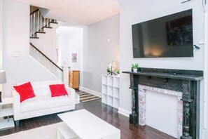 A modern living room with a staircase, a fireplace, and a mounted TV.