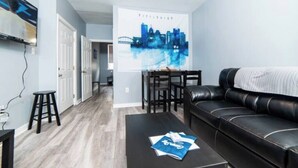 Ein Wohnzimmer mit einer schwarzen Ledersofa, einem Couchtisch mit Zeitschriften, einem Essbereich mit Tisch und Stühlen und einem Stadtplakats an der Wand.
