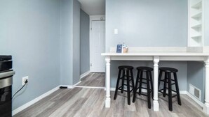 Eine Küche mit einer weißen Arbeitsplatte, drei schwarzen Barhocker und einer weißen Tür im Hintergrund.