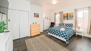 Ein Schlafzimmer mit einem Bett, einem Schminktisch, einem Sessel, einem Schreibtisch und einem Deckenventilator.