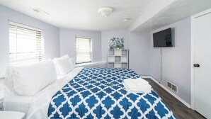 A bedroom with a bed, two windows, a TV, and a white door. - ROKU TVs - Washer & Dryer - QueenBeds - GroupStay (Pittsburgh)
