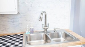 A kitchen with two stainless steel sinks, a faucet, a checkered mat, and a white cabinet. - ROKU TVs - Washer & Dryer - QueenBeds - GroupStay (Pittsburgh)