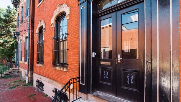 A red brick building with a black door labeled '1307,' a small window with a metal grill, and a narrow sidewalk. - ROKU TVs - Washer & Dryer - QueenBeds - GroupStay (Pittsburgh)