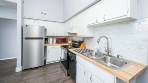 A modern kitchen with white cabinets, stainless steel appliances, a wooden countertop, and a tiled backsplash. - ROKU TVs - Washer & Dryer - QueenBeds - GroupStay (Pittsburgh)