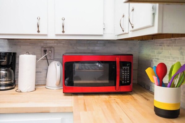 Una cocina con un microondas rojo, una cafetera, un hervidor y una taza con utensilios de colores.