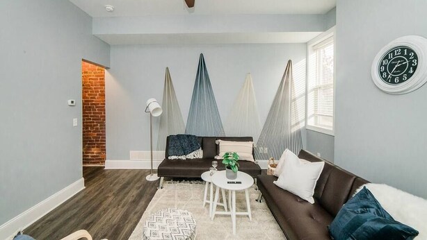 Ein Wohnzimmer mit Deckenventilator, einem braunen Sofa, einem weißen Couchtisch und einer Ziegelwand.
