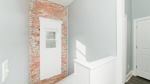 Ein Flur mit Backsteinwand, einer weißen Tür und einem weißen Geländer.