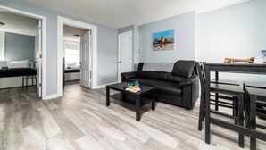 A living room with a black sofa, a coffee table, and a dining area with a table and chairs. - -- AGH Walkable - Free Parking - Washer & Dryer -- (Pittsburgh)