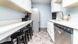 A compact kitchen with a refrigerator, dishwasher, bar stools, and a coffee maker. - -- AGH Walkable - Free Parking - Washer & Dryer -- (Pittsburgh)