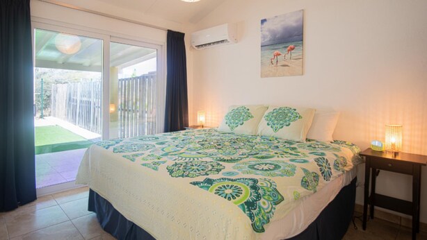 A bedroom with a bed, a nightstand, a wall-mounted air conditioner, and a painting of a beach scene. - NEW Casa Orcuyo in Santa Cruz (Santa Cruz)