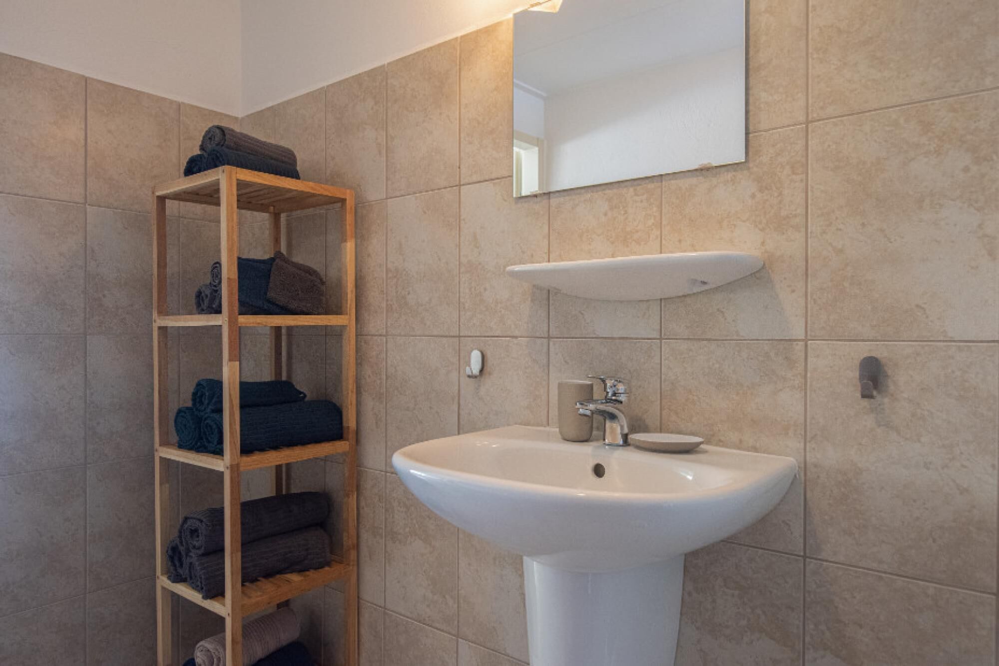 A bathroom with a wooden shelf holding towels, a white sink, and a mirror above it.