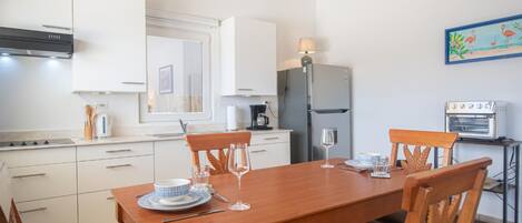 A modern kitchen with white cabinets, a wooden dining table, and a built-in oven.