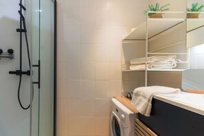Enjoy a refreshing shower in this sleek bathroom with a glass enclosure, washing machine, and mirrored cabinet.