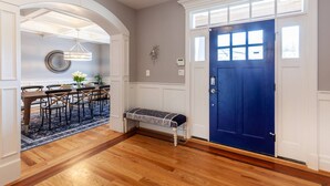 Un pasillo con piso de madera, una puerta azul y una zona de comedor con mesa y sillas.