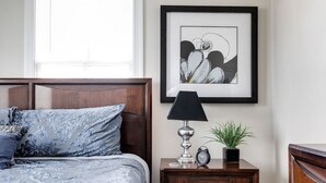 A bedroom with a bed, a bedside table with a lamp, a framed picture, and a small potted plant. - Modern, Convenient Gem: Urban Retreat 'n Richmond (Richmond)
