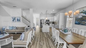 A modern kitchen with white cabinets, a central island, and a dining area with a wooden table and white chairs.