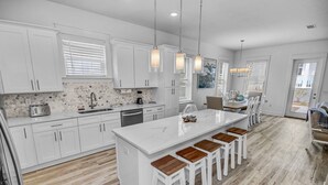 A modern kitchen with white cabinetry, a central island with bar stools, and pendant lighting.