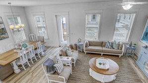 A spacious living room with a wooden dining table, white chairs, a beige sofa, and a round coffee table.