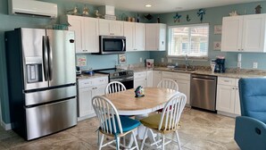 A compact kitchen with white cabinets, a stainless steel refrigerator, a microwave, and a coffee maker. There is a dining table with four chairs. - Beachgate Condo Suites And Hotel 231 1 Bedroom Condo (Port Aransas)