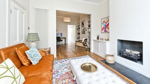 A living room with a brown sofa, a patterned rug, a white ottoman, a fireplace, and a bookshelf. - Family Home near Clapham Common (London)