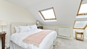 A bedroom with a large bed, a skylight, a radiator, and a small wooden table. - Family Home near Clapham Common (London)