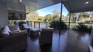 A covered outdoor deck with wicker furniture, a dining area, and a view of a lake. - Lily Pad Beach House (Agnes Water)