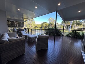 A covered outdoor area with wicker furniture, a view of trees, and a clear sky. - Lily Pad Beach House (Agnes Water)