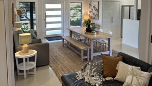 A spacious living area with a black leather sofa, a wooden dining table, and a kitchen in the background. - Lily Pad Beach House (Agnes Water)
