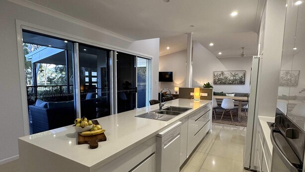 A modern kitchen with a large island, built-in appliances, and a view to an outdoor area. - Lily Pad Beach House (Agnes Water)