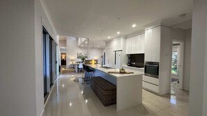 A modern kitchen with white cabinets, a central island, and stainless steel appliances. - Lily Pad Beach House (Agnes Water)