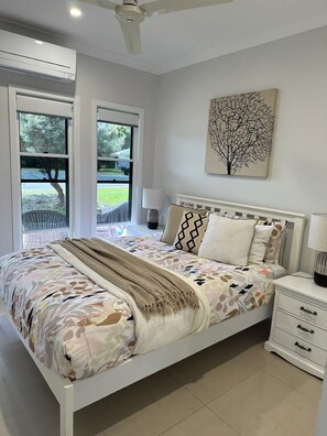 A bedroom with a bed, bedside tables, a ceiling fan, and a window with a view of the outdoors. - Lily Pad Beach House (Agnes Water)