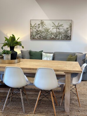 A dining area with a wooden table, two white chairs, a grey sofa, and a wall-mounted plant. - Lily Pad Beach House (Agnes Water)