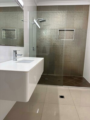 A modern bathroom with a white vanity, a glass shower enclosure, and a textured wall. - Lily Pad Beach House (Agnes Water)