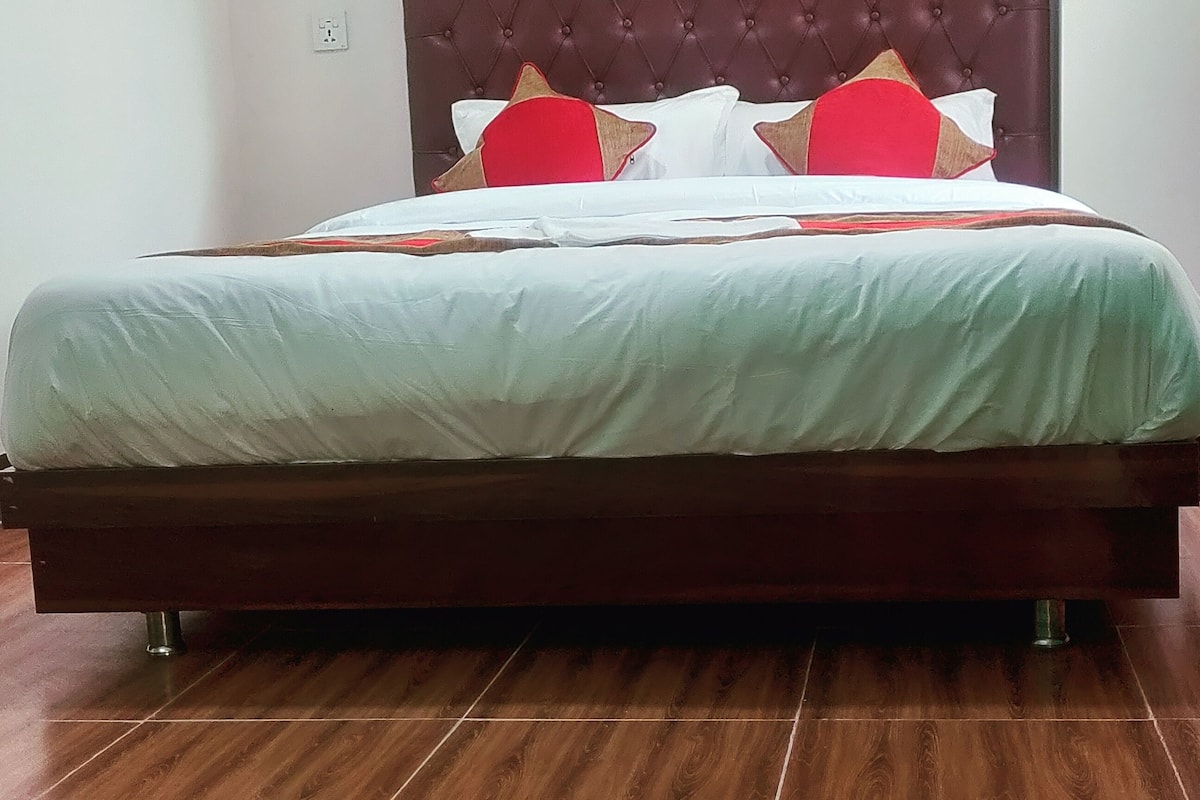 Una cama bien hecha con cabecera de madera y almohada roja decorativa.