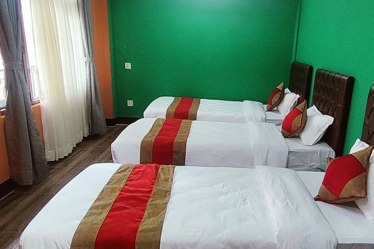 Habitación de hotel con tres camas, cada una con ropa de cama blanca y detalles en rojo y dorado. Las paredes son verdes y el piso es de madera.