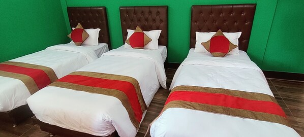 A hotel room with three beds, each with a red and white bedspread and matching pillows. The room has green walls and a wooden floor.