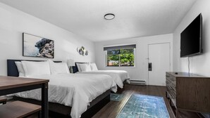 Une chambre moderne avec deux lits, une télévision, un bureau et une fenêtre donnant sur un paysage verdoyant.