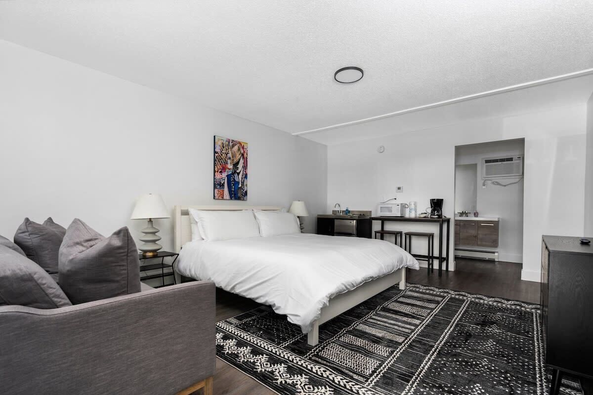 Ein modernes Schlafzimmer mit einem Bett, Nachttischen, einem Schreibtisch und einer Küchenzeile.