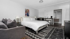 A modern bedroom with a bed, bedside tables, a desk, and a kitchenette. - King Studio TC | Near Downtown + Near beach (Traverse City)