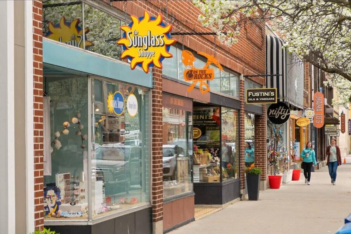 A storefront with a large sunburst sign for 'The Sunglass Shoppe' and another sign for 'Fustini's Oils & Vinegars'.