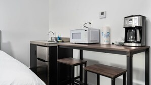 A compact hotel room with a kitchenette, including a microwave, coffee maker, and a small refrigerator. There is a sink with a faucet, and a single stool is placed at the counter. - Peninsula One Apartments Unit 17 (Traverse City)