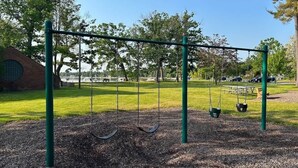 A playground with swings and a brick building in the background. - Peninsula One Apartments Unit 17 (Traverse City)