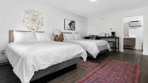 A hotel room with two beds, a desk, a chair, a red patterned rug, and a wall-mounted air conditioner. - Peninsula One Apartments Unit 21 (Traverse City)