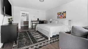 Une chambre d’hôtel moderne avec un grand lit, un bureau, un téléviseur à écran plat, un fauteuil gris et une peinture abstraite aux couleurs vives accrochée au mur.